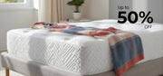 White mattress with a colorful blanket on a bed in a room with a window and plant.